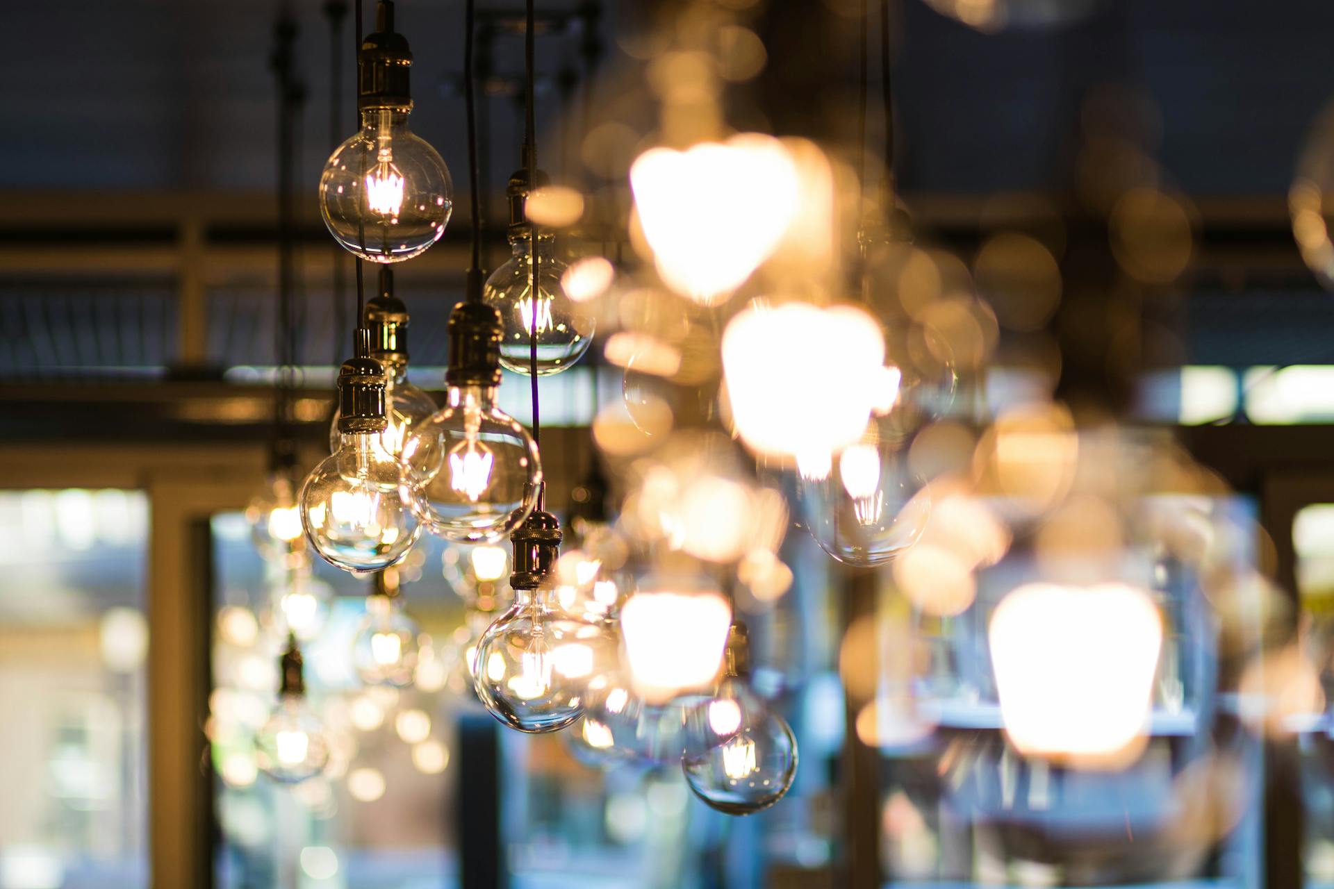 Light bulbs hanging from a ceiling. Some are in focus, and look like old-fashioned filament round bulbs. Others are out of focus, and could be different kinds of light bulbs.