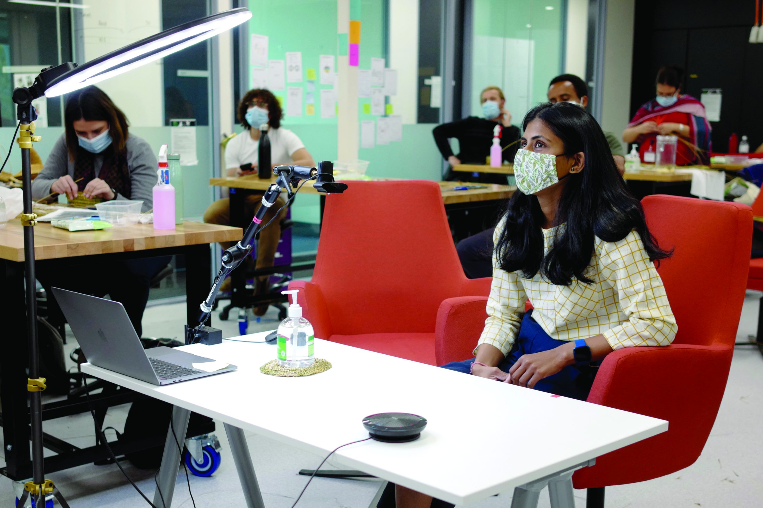 Students sitting at desks in a classroom. They are all wearing masks. In the foreground is a student with long dark hair, looking up towards the front of the room. Her face mask is made from green and white printed cloth.